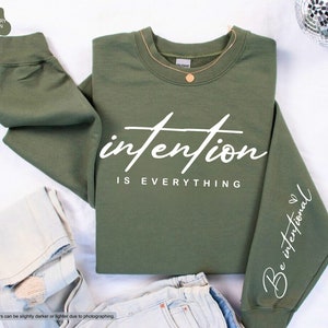 May include: A green sweatshirt with the text "intention is everything" in white on the front and "Be intentional" in white on the sleeve.