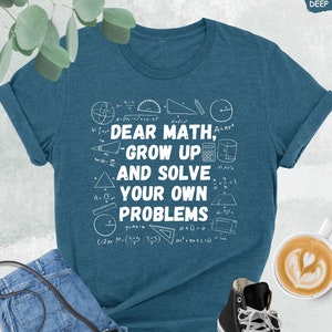 May include: A teal blue t-shirt with a white graphic that says "Dear Math, Grow Up and Solve Your Own Problems" surrounded by math symbols and equations.