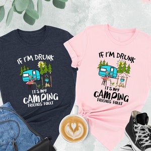 May include: Two t-shirts with a camping theme. The blue shirt says "If I'm Drunk It's My Camping Friends Fault". The pink shirt says "If I'm Drunk It's My Camping Friends Fault". Both shirts feature a cartoon camper, a flamingo, and a campfire.