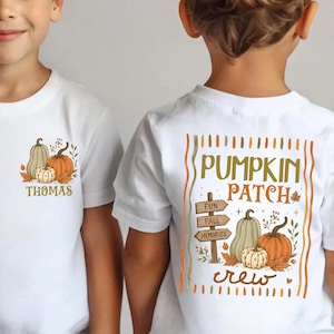 May include: A white short-sleeved t-shirt featuring a small pumpkin graphic on the front left chest with the name Thomas. The back displays a large graphic with the text Pumpkin Patch, a signpost reading Fun, Fall, Memories, and pumpkins.