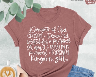 May include: A heather mauve t-shirt with the text "Daughter of God CHOSEN + Treasured created for a purpose set apart + REDEEMED pursued + FORGIVEN Kingdom girl" in white lettering.