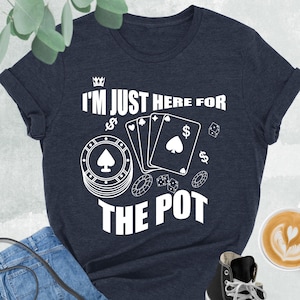 May include: Heather navy t-shirt with the text "I'M JUST HERE FOR THE POT" and poker-themed graphics. The image includes blue jeans, a black purse, and black high-top sneakers. A cup of coffee with latte art is also visible.