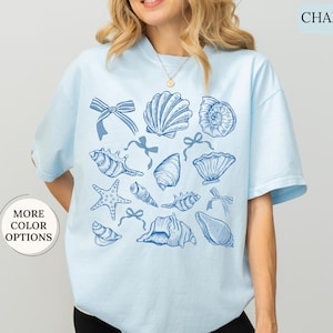 May include: A light blue t-shirt with a pattern of blue seashells and bows. The text "CHAMBRAY" is in the top right corner of the image.