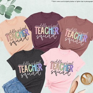 Może przedstawiać: Prezentacja pięciu koszulek w różnych kolorach, w tym brzoskwiniowym, bordowym i ciemnoszarym. Każda koszulka zawiera napis "middle school TEACHER squad" w kolorowej, obrysowanej czcionce. Widoczne są również dżinsy, buty i filiżanka kawy.