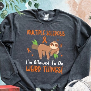 May include: Dark heather grey sweatshirt with a sloth wearing an orange ribbon and the text "Multiple Sclerosis & I'm Allowed To Do Weird Things!"