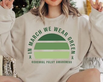 Può includere: Una felpa beige chiaro con una grafica verde che dice "In March We Wear Green" e "Cerebral Palsy Awareness".