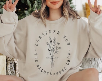 May include: A beige sweatshirt with a black circle graphic that says "Consider how the wildflowers grow."  The graphic also includes a bouquet of wildflowers and the text "Luke 12:27".