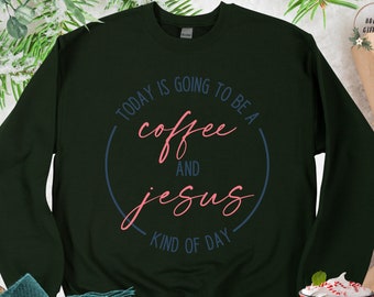 May include: A dark green sweatshirt with the text "TODAY IS GOING TO BE A coffee AND jesus KIND OF DAY" in a circle. The text is in a white font with a blue outline. The sweatshirt is on a table with a red mug and a gift box.