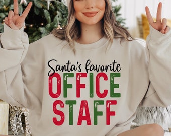 May include: A beige sweatshirt with the text "Santa's favorite OFFICE STAFF" in red and green letters. The letters have a distressed look.