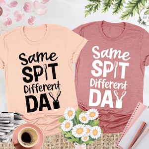 May include: Two t-shirts with a dental theme. One is peach colored with black text that says "Same Spit Different Day" and the other is a dusty rose color with white text that says "Same Spit Different Day". Both shirts have a graphic of a toothbrush and toothpaste.
