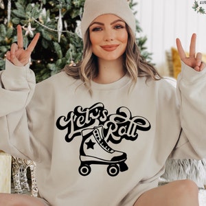 May include: A beige sweatshirt with a black graphic of a roller skate and the text "Let's Roll" in a retro font.