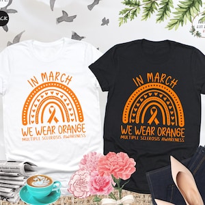 May include: Two t-shirts with a rainbow design and the text "In March We Wear Orange" and "Multiple Sclerosis Awareness".