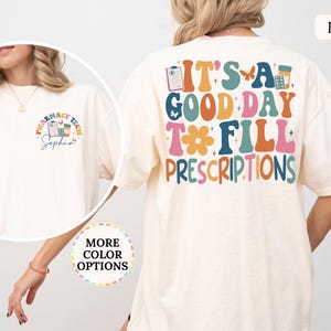 May include: Ivory-colored t-shirt with the text "IT'S A GOOD DAY TO FILL PRESCRIPTIONS" in colorful, retro-style lettering on the back. The front features a pharmacy tech graphic. The shirt is a comfortable, oversized fit.