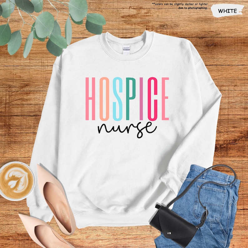 K&ouml;nnte beinhalten: Wei&szlig;er Pullover mit dem Text "Hospice nurse" in Regenbogenfarben.