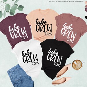 May include: Five t-shirts in different colors with the text "tube crew 2025" printed in white on the front. The shirts are laid out on a light brown surface.