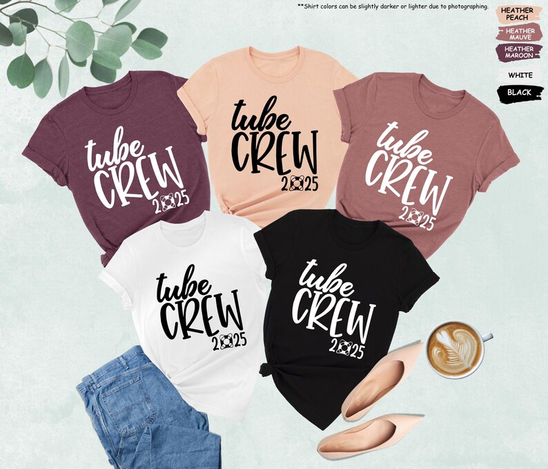 May include: Five t-shirts in different colors with the text "tube crew 2025" printed in white on the front. The shirts are laid out on a light brown surface.