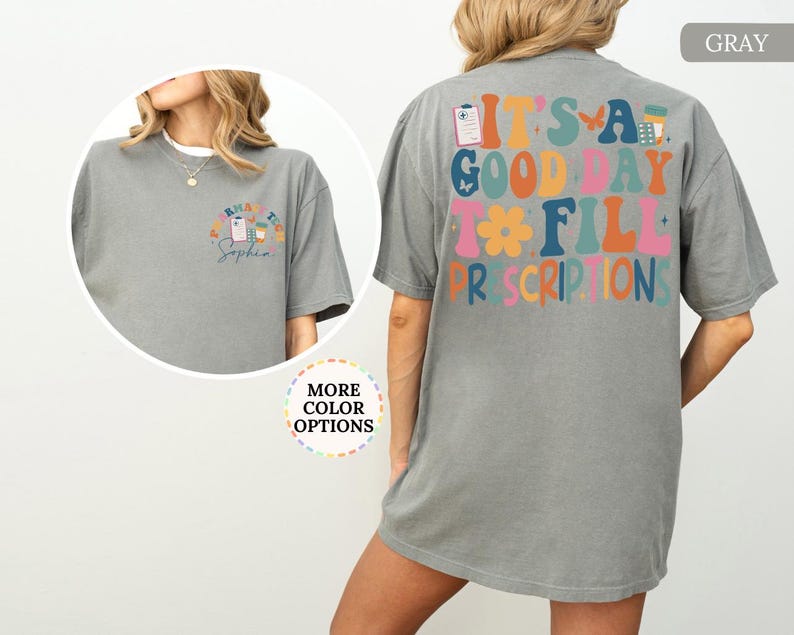 May include: A grey t-shirt featuring the phrase "IT'S A GOOD DAY TO FILL PRESCRIPTIONS" in a colourful, retro font on the back. The front displays a smaller design with a prescription pad, coffee cup, and the name "Sophia".