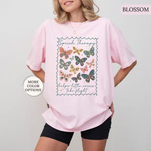 Puede incluir: Camiseta rosa claro con un dise&ntilde;o de mariposas coloridas y el texto "Speech Therapy helps little voices take flight" en un marco decorativo. La camiseta tiene un corte holgado.