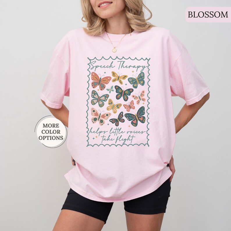 Puede incluir: Camiseta rosa claro con un dise&ntilde;o de mariposas coloridas y el texto "Speech Therapy helps little voices take flight" en un marco decorativo. La camiseta tiene un corte holgado.