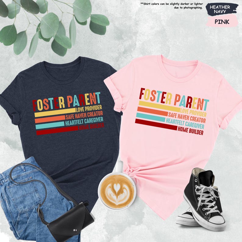 May include: Two t-shirts with the text "Foster Parent" in a retro style with colorful stripes. The text is layered with the words "Love Provider", "Safe Haven Creator", "Heartfelt Caregiver", and "Home Builder". One shirt is heather navy and the other is pink.