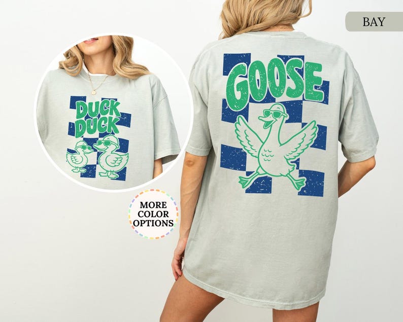 May include: A light gray short-sleeve t-shirt featuring a blue and green checkered pattern with a graphic of a goose wearing sunglasses and the text GOOSE on the back, and a smaller graphic of two ducks with the text DUCK DUCK on the front.