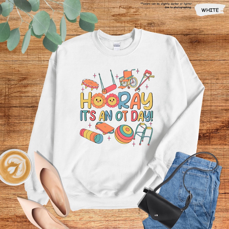 Peut inclure: Sweat-shirt blanc avec un motif graphique color&eacute; repr&eacute;sentant des outils d'ergoth&eacute;rapie et le texte "HOORAY IT'S AN OT DAY!"