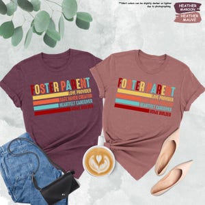 May include: Two heather colored t-shirts with the text "Foster Parent" in white and a colorful stripe design. The text below the stripes reads "Love Provider, Safe Haven Creator, Heartfelt Caregiver, Home Builder".