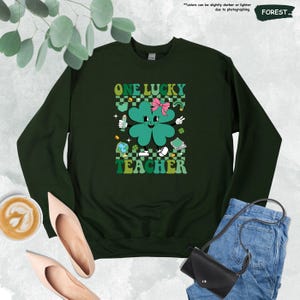 May include: Green sweatshirt with a four-leaf clover graphic and the text "ONE LUCKY TEACHER" in a retro style.