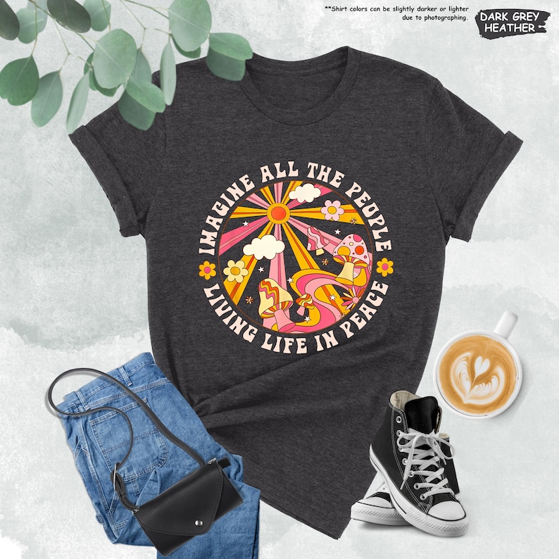May include: Dark grey heather t-shirt with a retro-style graphic of a sun, clouds, mushrooms, and flowers. The graphic has the text "Imagine All The People Living Life In Peace".