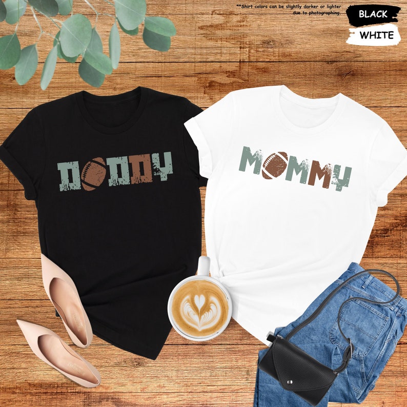 May include: Two black and white t-shirts with the words "Daddy" and "Mommy" printed on them. Each shirt has a football graphic.