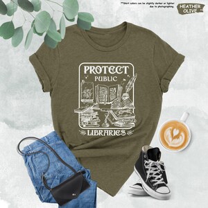 May include: A green t-shirt with a white graphic design that says "Protect Public Libraries". The graphic features a stack of books, a quill pen, and a magnifying glass.