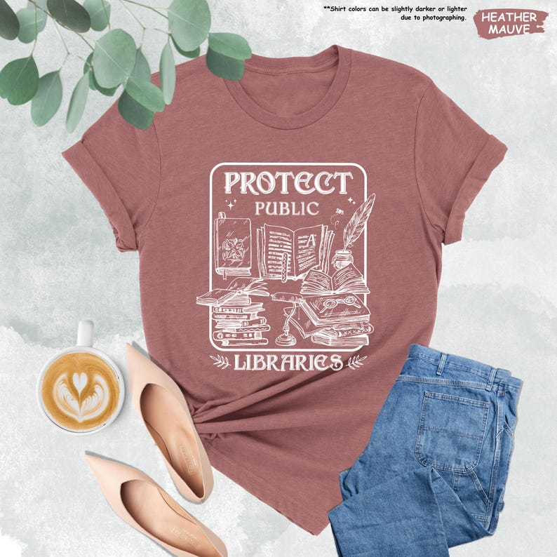 May include: A heather mauve t-shirt with a white graphic design that says "Protect Public Libraries" with an illustration of books, a quill pen, and a bottle of ink.