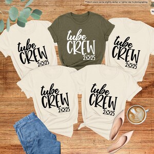 May include: Four white t-shirts with black text that reads "tube crew 2025". One of the shirts is olive green.