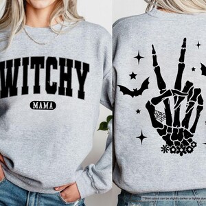 a woman wearing a grey sweater with a witch hand on it