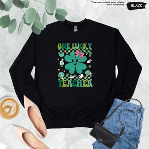 May include: Black sweatshirt with a green four-leaf clover graphic and the text "ONE LUCKY TEACHER".
