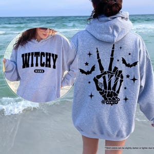 a woman wearing a witches hand hoodie on the beach