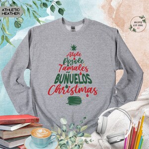 May include: Gray sweatshirt with a green Christmas tree design. The tree is made up of the words "Atole", "Pozole", "Tamales", "Bunuelos", and "Christmas".