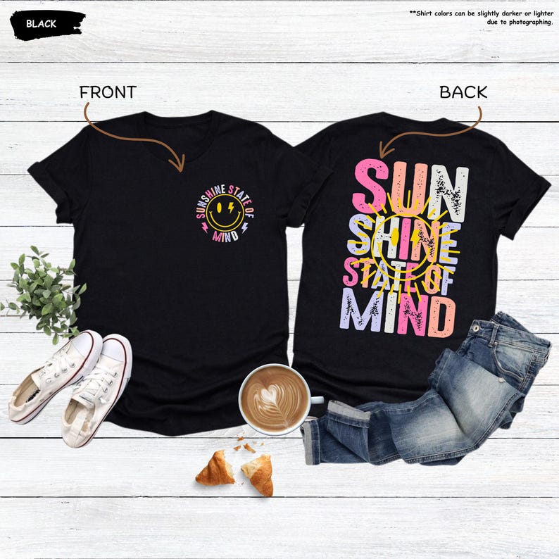 Pu&ograve; includere: T-shirt nero con scollo a V con grafica frontale di una faccia sorridente e le parole "Sunshine State of Mind". La parte posteriore della maglietta presenta le parole "Sun Shine State of Mind" in un design colorato e stratificato. Sono visibili anche scarpe da ginnastica bianche e jeans.