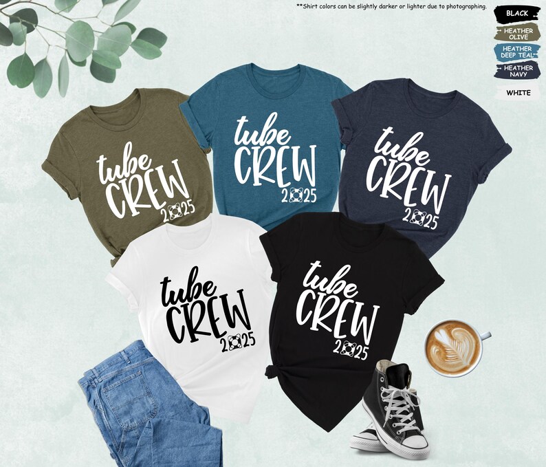 May include: Five t-shirts in different colors with the text "tube crew 2025" printed in white on each shirt. The shirts are laid out on a white surface with a cup of coffee and a pair of sneakers.