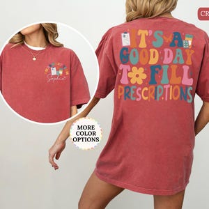 May include: Crimson t-shirt featuring the text "IT'S A GOOD DAY TO FILL PRESCRIPTIONS" in various colours on the back. The front displays a smaller pharmacy-themed graphic with the text "Pharmacy Sophia".