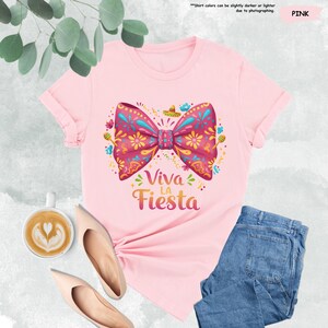 Może przedstawiać: R&oacute;żowa koszulka z kolorową kokardką i napisem "Viva la Fiesta".
