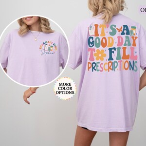 May include: Orchid-coloured t-shirt with the text "IT'S A GOOD DAY TO FILL PRESCRIPTIONS" on the back. The front of the shirt has a pharmacy tech logo and the name "Sophia". The shirt is a comfortable, casual style.
