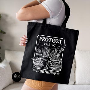 May include: Black tote bag with white text and graphic. The text reads "Protect Public Libraries" and the graphic depicts a stack of books with a quill pen.