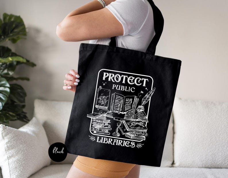 May include: Black tote bag with white text and graphic. The text reads "Protect Public Libraries" and the graphic depicts a stack of books with a quill pen.