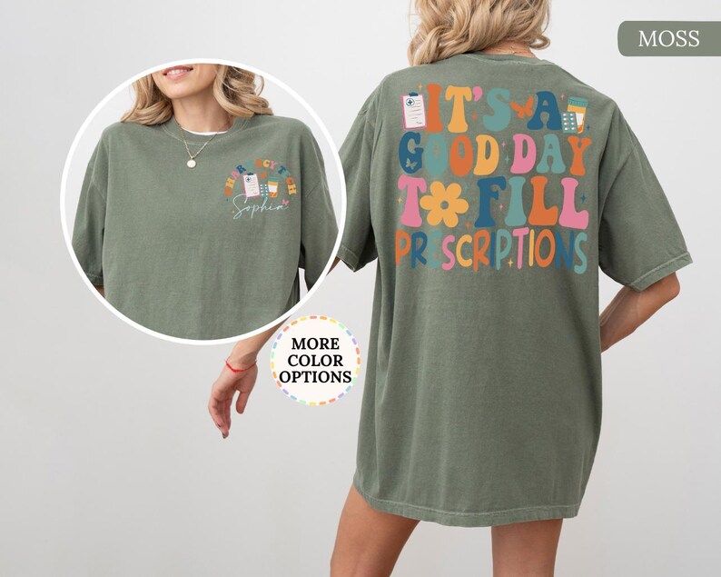 May include: A moss green t-shirt with the phrase "IT'S A GOOD DAY TO FILL PRESCRIPTIONS" in colourful, retro lettering on the back. The front has a smaller design with the text "HAPPY CV TECH" and a name. A relaxed, comfortable style.