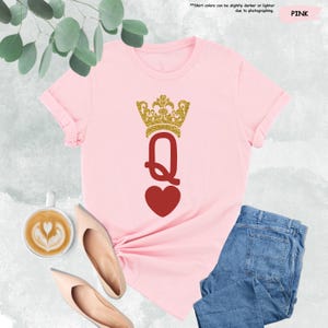 Puede incluir: Camiseta rosa con una corona dorada de purpurina y un coraz&oacute;n rojo con la letra Q en el centro. La camiseta est&aacute; sobre una superficie blanca con una taza de caf&eacute; y un par de zapatos.