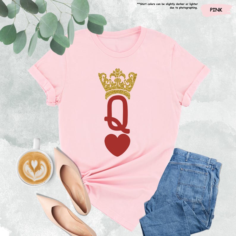 Puede incluir: Camiseta rosa con una corona dorada de purpurina y un coraz&oacute;n rojo con la letra Q en el centro. La camiseta est&aacute; sobre una superficie blanca con una taza de caf&eacute; y un par de zapatos.
