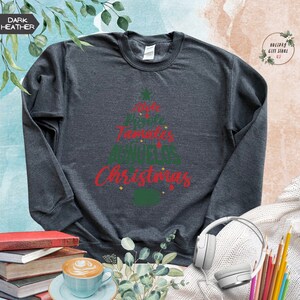 May include: Dark heather grey sweatshirt with a Christmas tree design. The tree is made of the words "Atole", "Posada", "Tamales", "Noche Buena", and "Christmas".