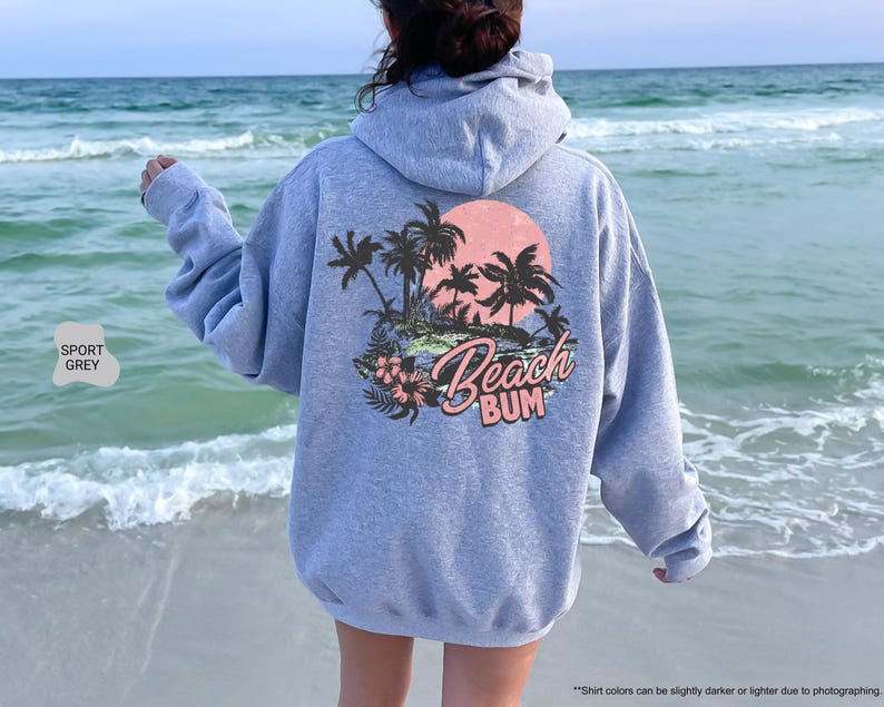 May include: Sport grey hoodie with a tropical beach scene graphic on the back, featuring palm trees, a sunset, and the words "Beach Bum". The hoodie has a drawstring hood and long sleeves.