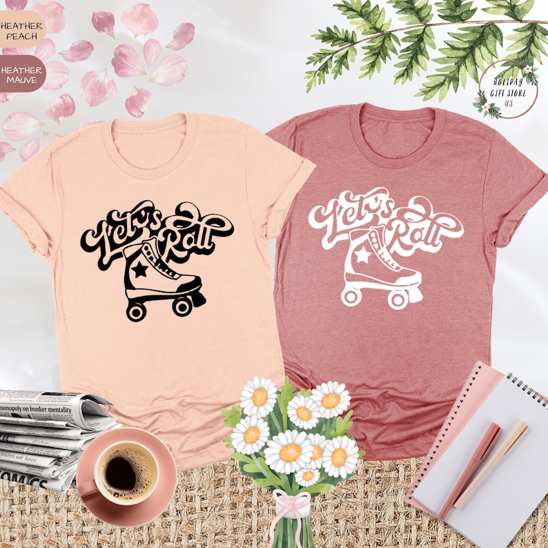 May include: Two t-shirts with the text "Let's Roll" in a retro font, with a roller skate graphic. The t-shirt on the left is peach colored and the t-shirt on the right is a dusty rose color.